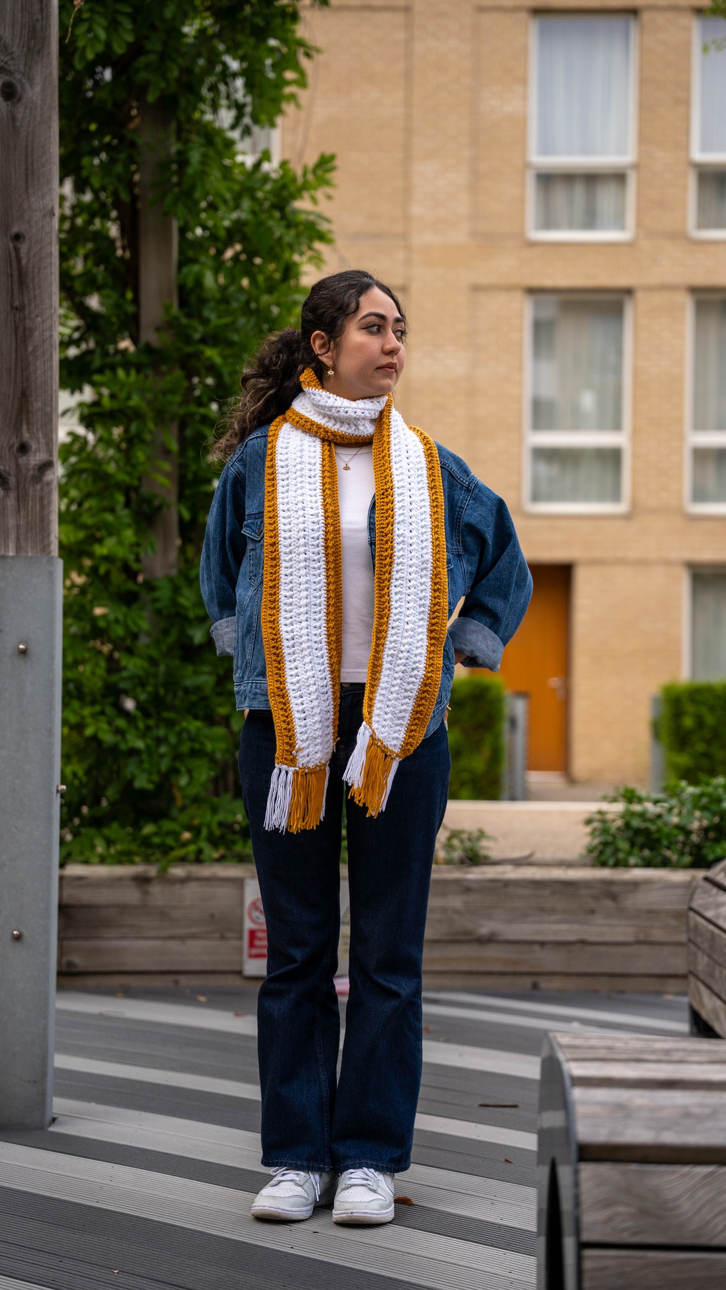 Model wearing mustard and white crochet scarf, back view on bench