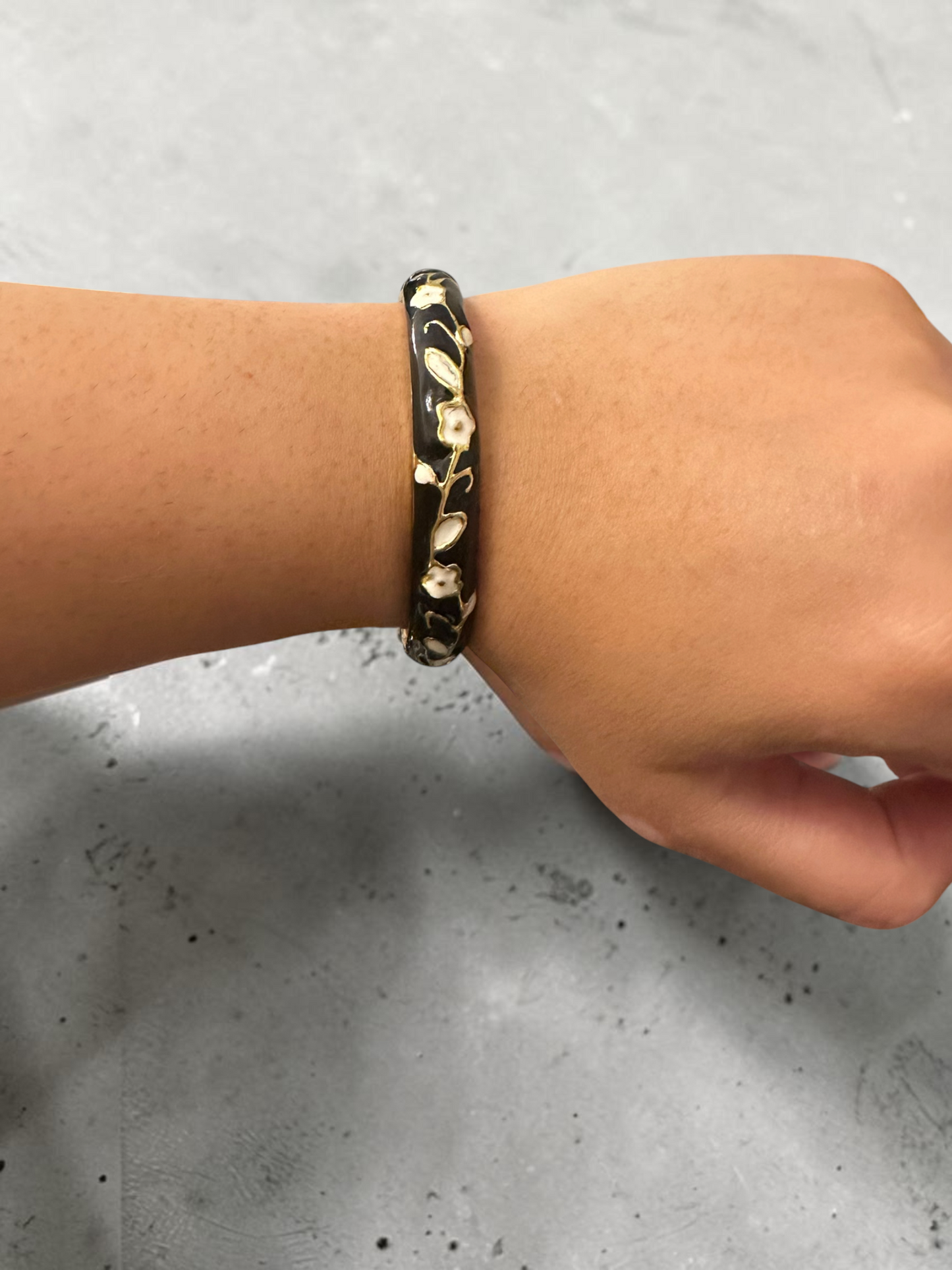 Black enamel floral bangle worn on wrist front view