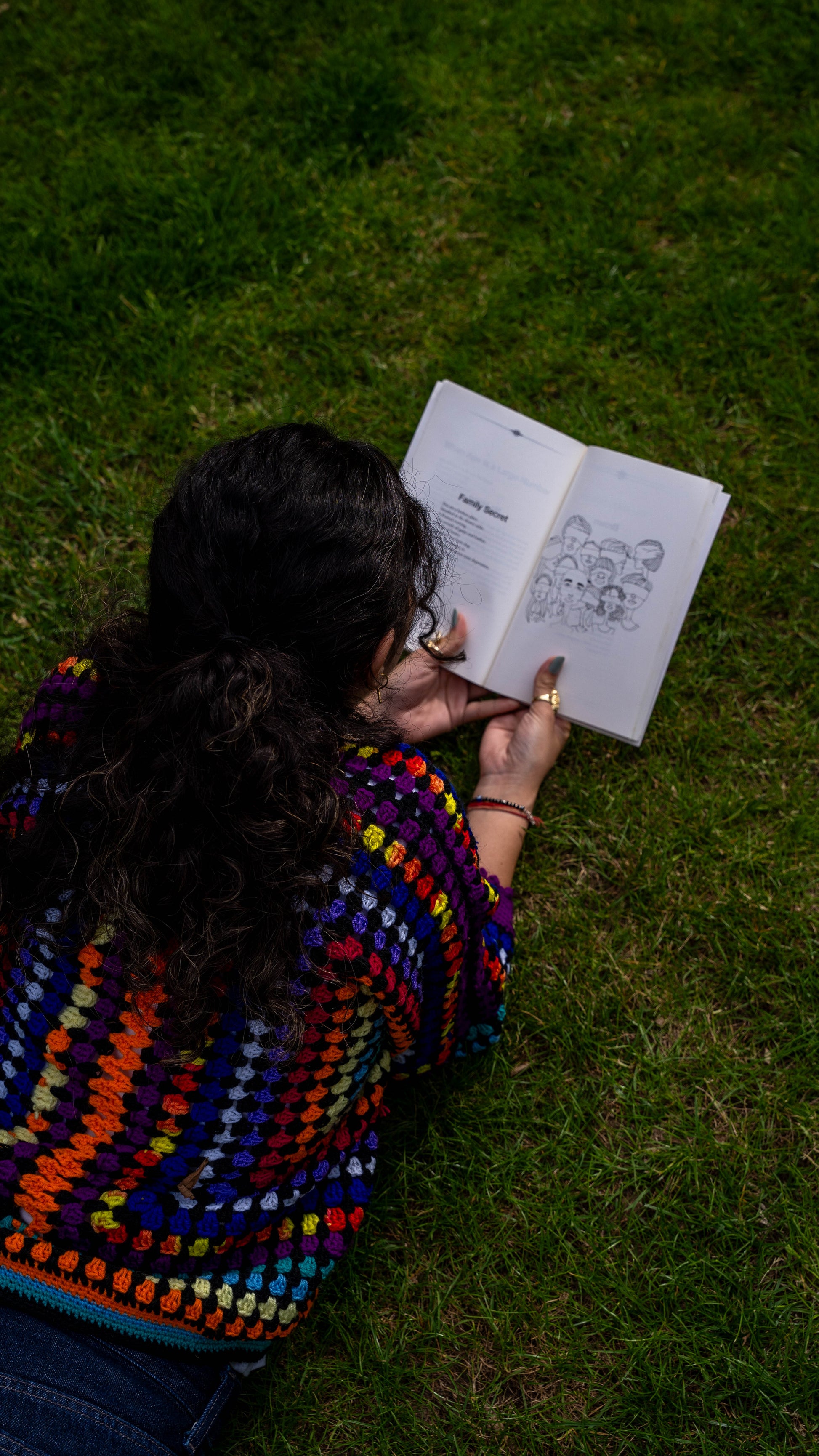 Model lying on grass wearing rainbow crochet cardigan, looking up