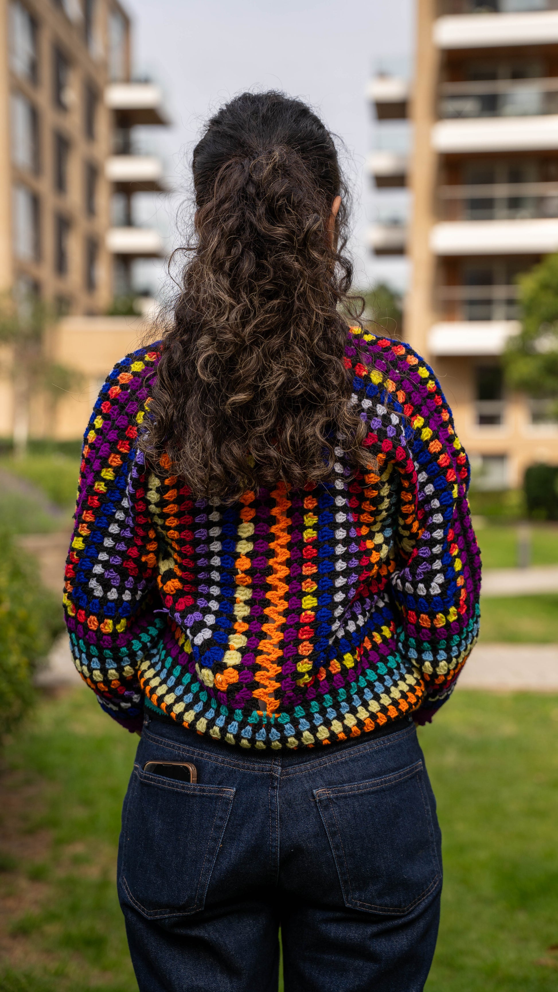 Model wearing rainbow granny square crochet cardigan, back view