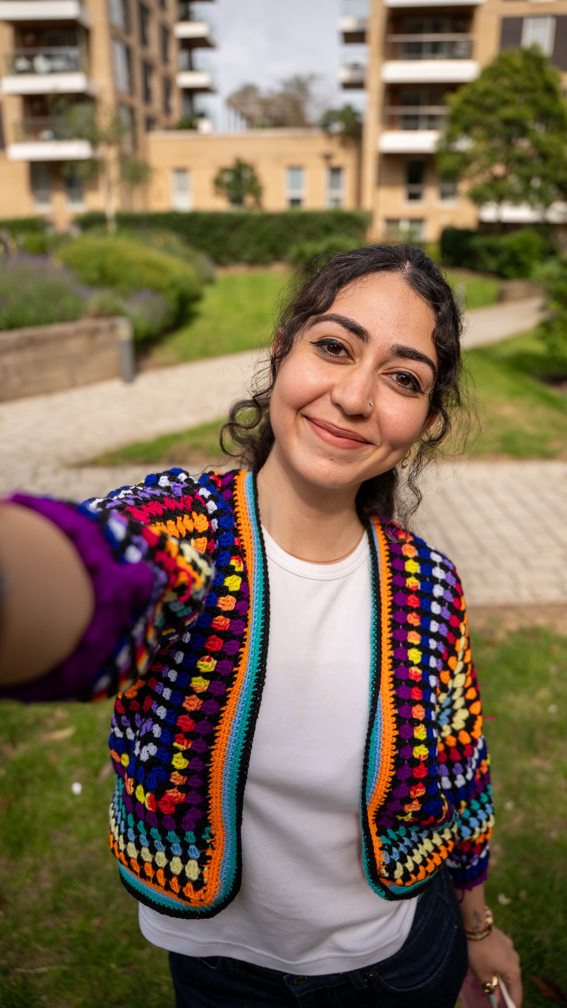 Model lying on grass wearing rainbow crochet cardigan, reading a book