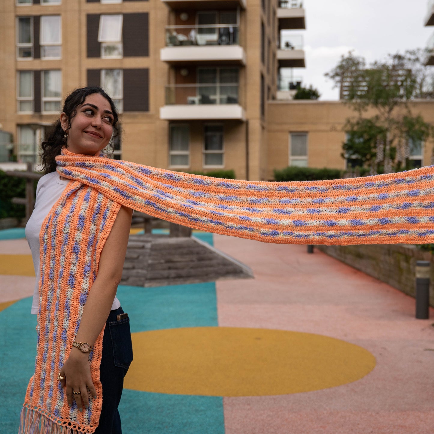 Model holding out peach and lilac crochet scarf showing full length