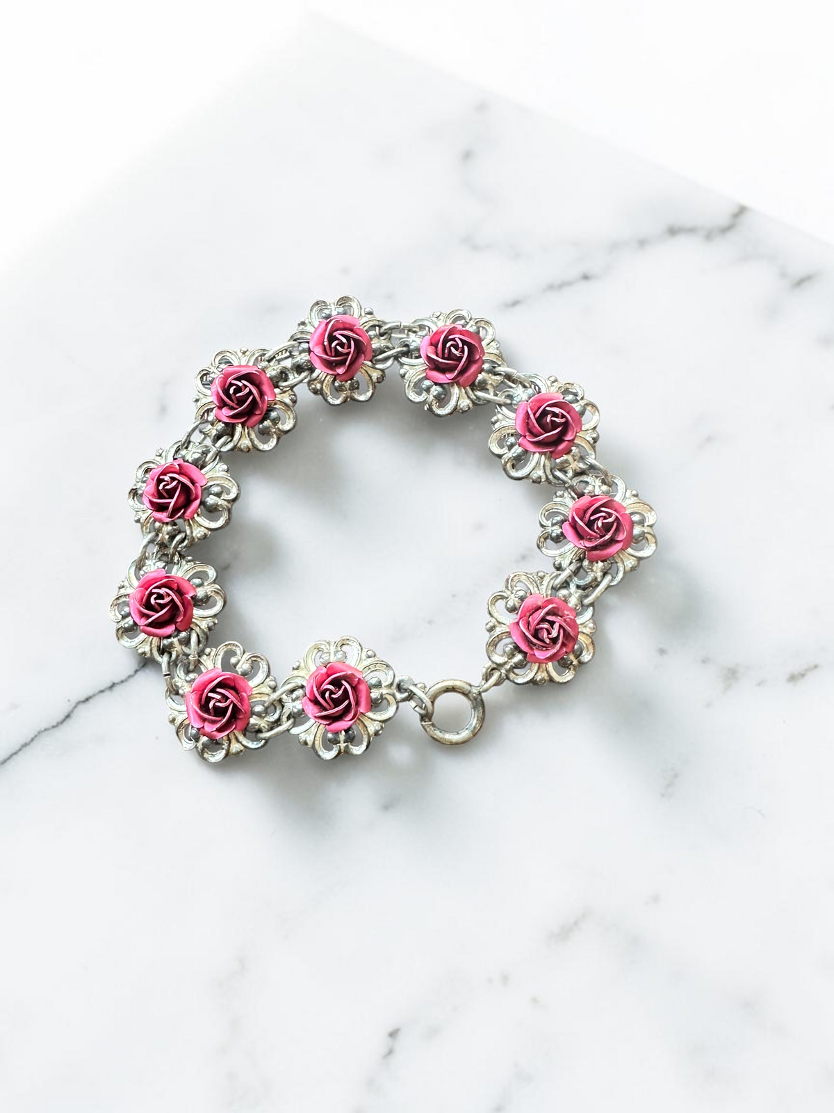 Vintage pink rose silver tone filigree link bracelet, overhead view on marble