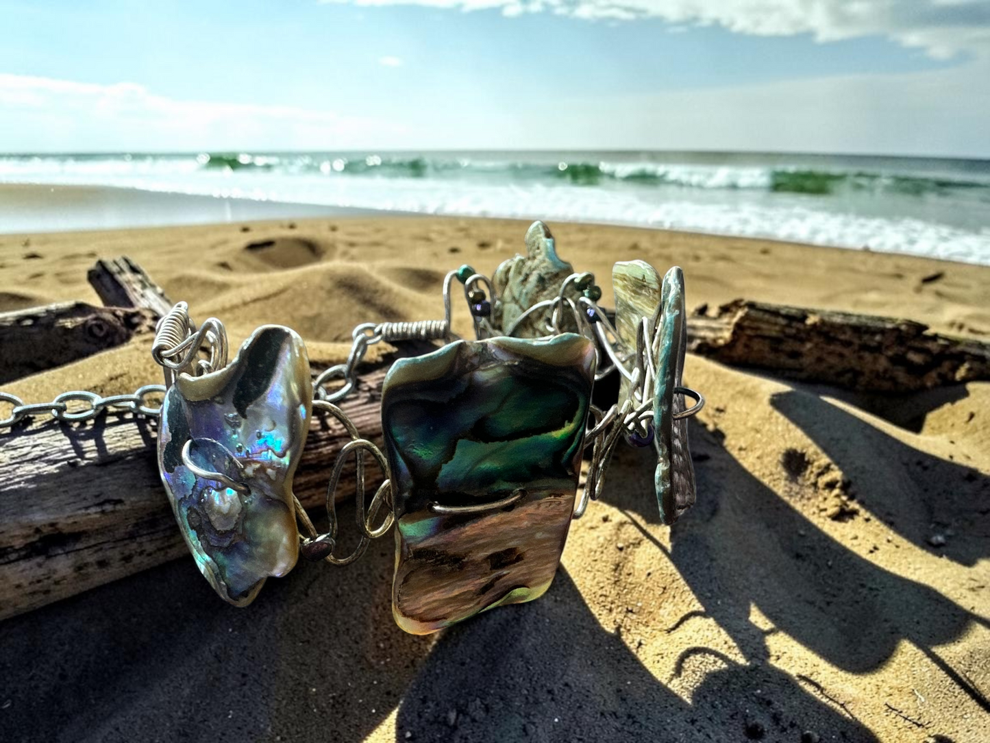 Handcrafted abalone shell wire wrapped bracelet displayed on driftwood at the beach