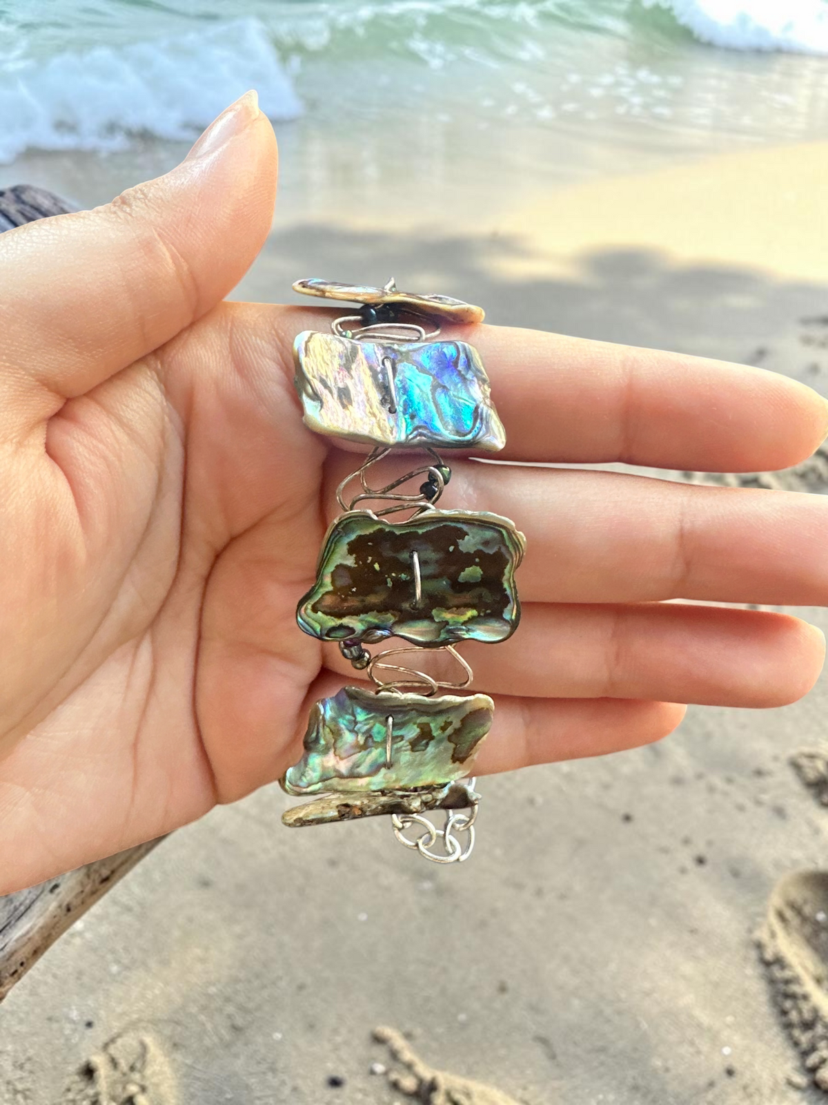 Handcrafted abalone shell wire wrapped bracelet held in hand showing iridescent detail