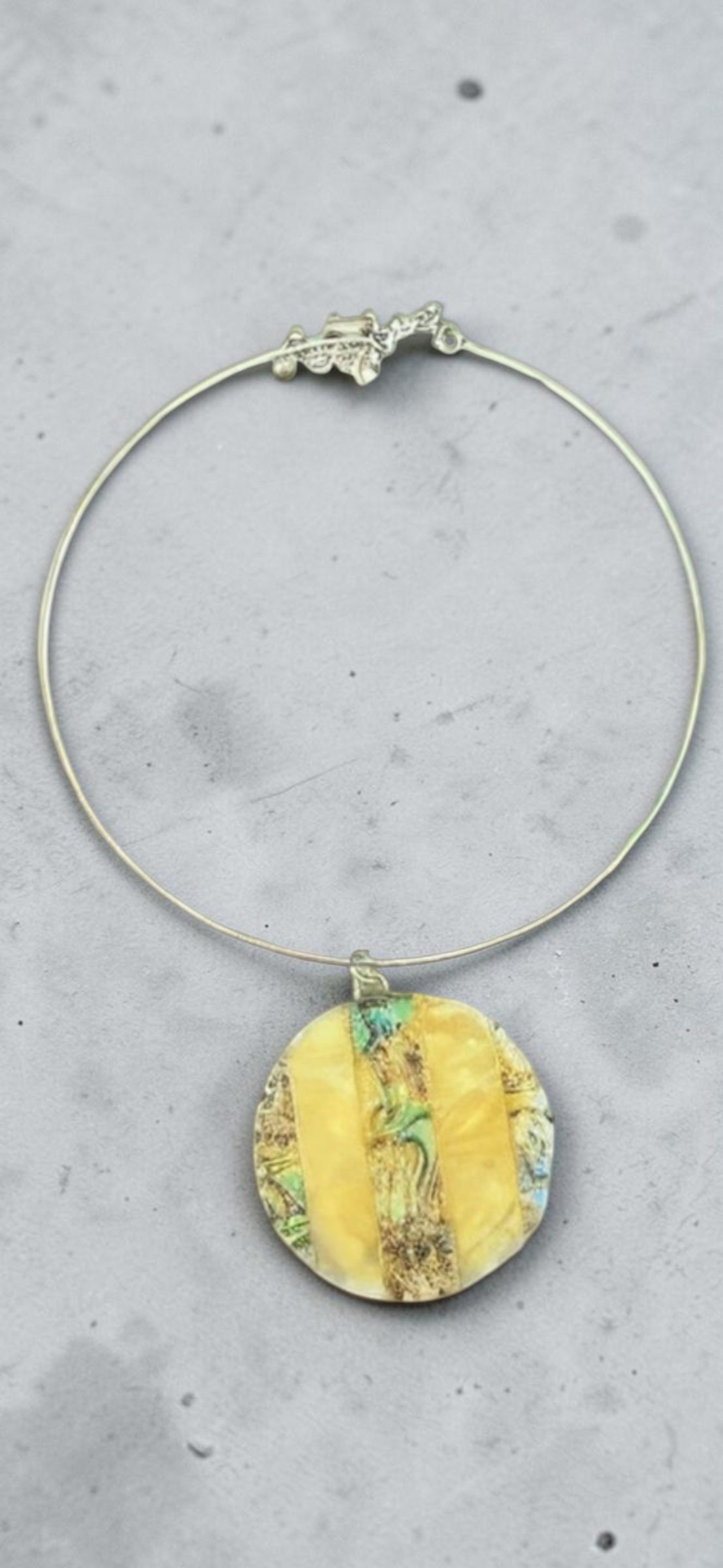 Yellow abalone shell disc choker necklace, close-up of pendant on concrete