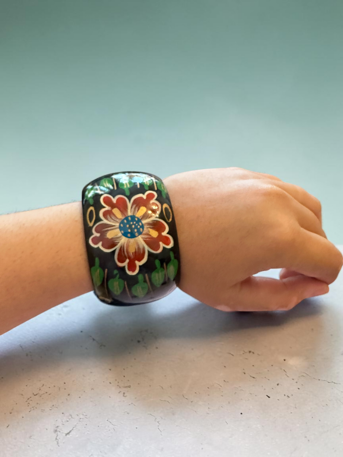 Hand-painted floral bangle worn on wrist, side angle showing full width of the cuff
