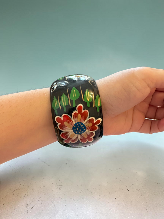 Hand-painted floral bangle worn on wrist, showing red flower with blue centre and green leaf motifs on black lacquer