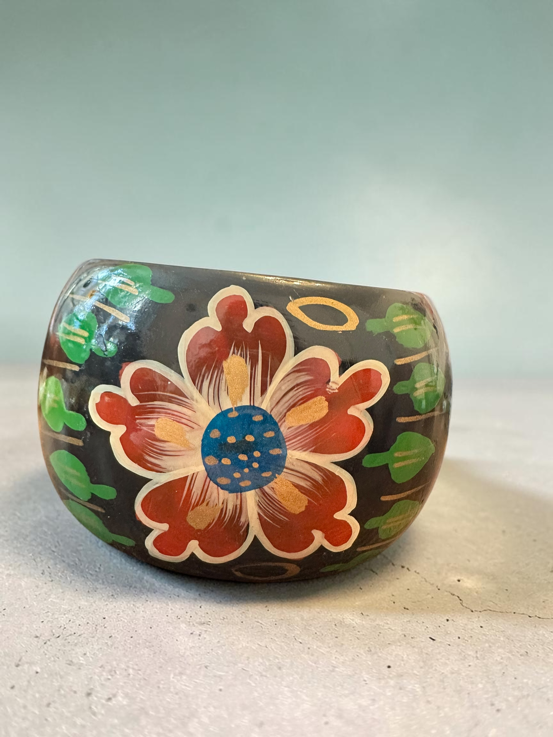 Close-up of hand-painted floral bangle showing detailed red flower and green leaf design on black lacquered base