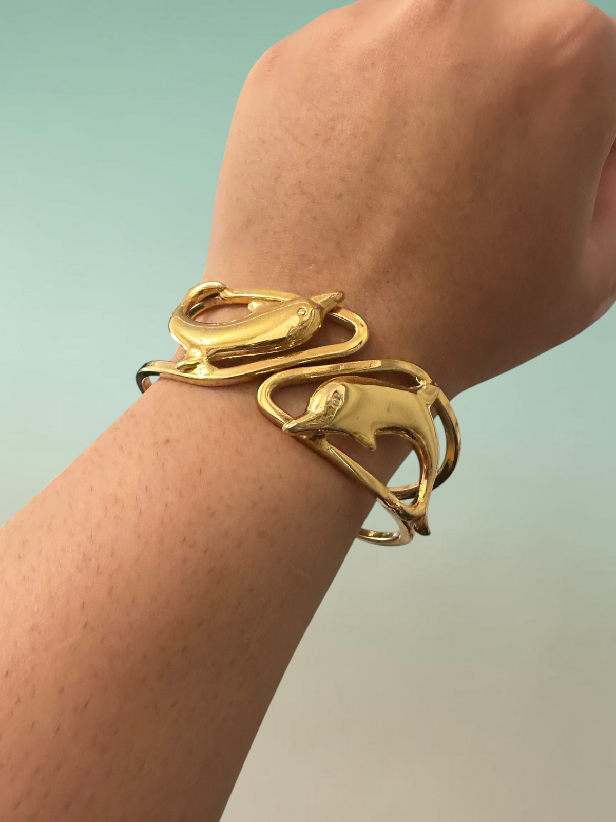 Gold tone dolphin cuff bracelet worn on wrist